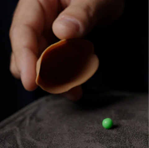 Top-down view of the 3 shell game trick in action on a close-up mat with hands mid-performance